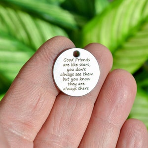 May include: A circular, silver-toned charm with a small hole at the top. The charm features the engraved quote: "Good Friends are like stars, you don't always see them but you know they are always there."