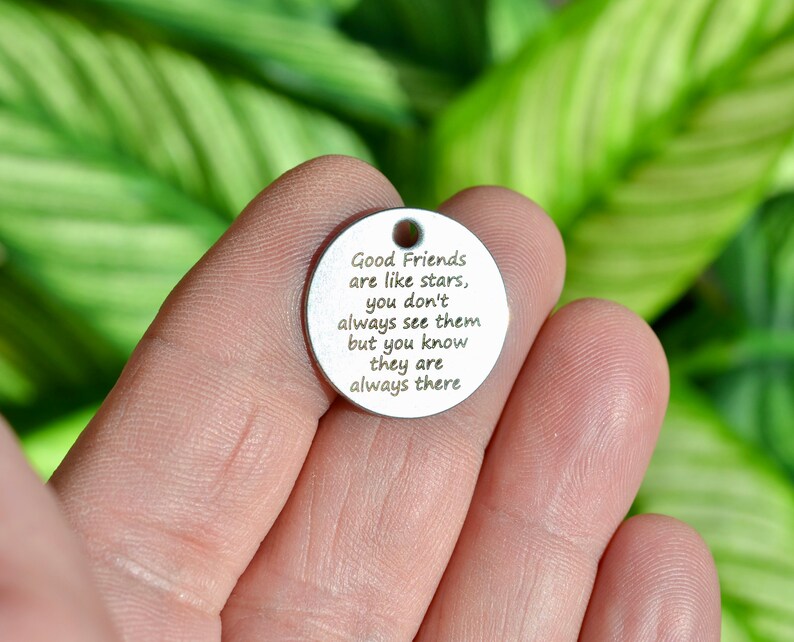 May include: A circular, silver-toned charm with a small hole at the top. The charm features the engraved quote: "Good Friends are like stars, you don't always see them but you know they are always there."