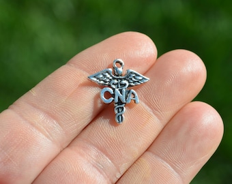 Könnte beinhalten: Silberner Anhänger mit einem Caduceus-Symbol und den Buchstaben CNA.
