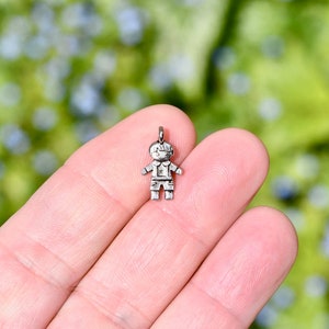May include: A silver charm in the shape of a small child. The charm is detailed with a face, arms, legs, and a shirt.