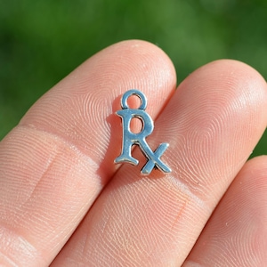 May include: Silver charm with the letter R and a cross, commonly used to represent a prescription.