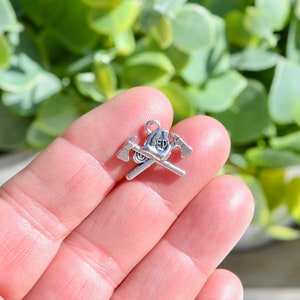 May include: Silver charm featuring a firefighter helmet with crossed axes.