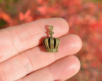 May include: A small gold-toned crown charm with a detailed design. The crown has a pointed top and a rounded base. It is a perfect embellishment for jewelry making or crafting projects.