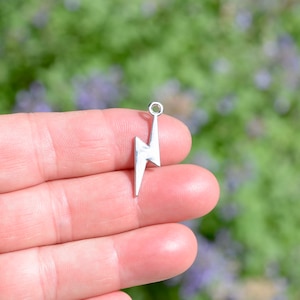 May include: Silver charm in the shape of a lightning bolt. The charm has a loop at the top for attaching to a necklace or bracelet.