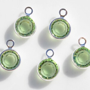 May include: Five silver charm pendants with green glass stones. Each pendant has a loop at the top for attaching to a chain or bracelet.