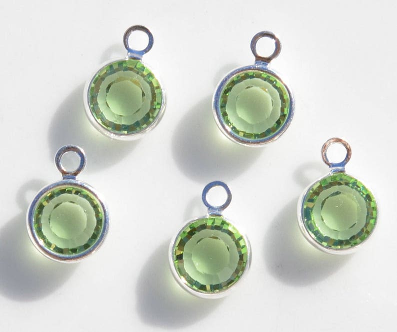 May include: Five silver charm pendants with green glass stones. Each pendant has a loop at the top for attaching to a chain or bracelet.