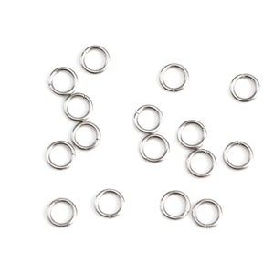 May include: A collection of silver jump rings, a type of jewelry finding, scattered on a white background.