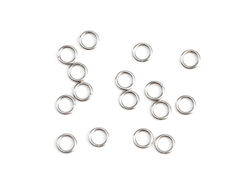May include: A collection of silver jump rings, a type of jewelry finding, scattered on a white background.