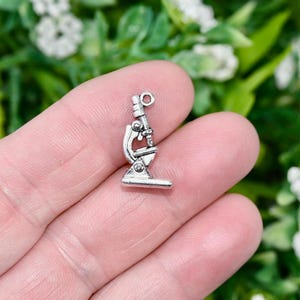May include: Silver-toned microscope charm with a detailed design. The charm has a loop at the top for attaching to a necklace or bracelet.