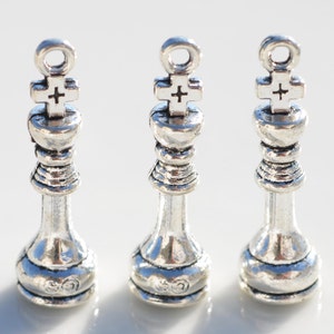 May include: Three silver chess king charms with a cross on top. The charms are about 2 inches tall and have a loop at the top for attaching to a necklace or bracelet.