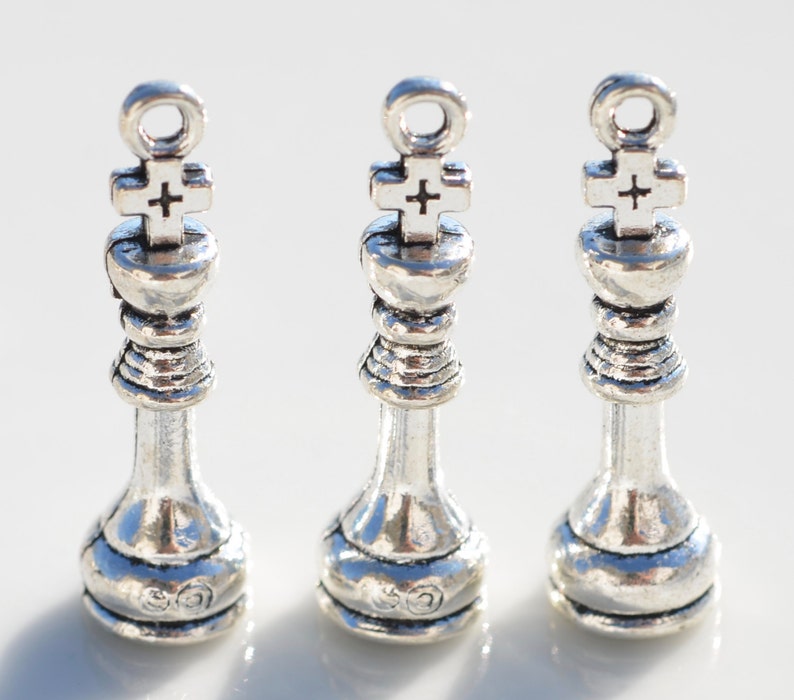 May include: Three silver chess king charms with a cross on top. The charms are about 2 inches tall and have a loop at the top for attaching to a necklace or bracelet.