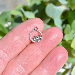 May include: Silver charm with a circle design featuring a wave pattern. The charm is small and delicate, perfect for adding a touch of whimsy to jewelry.