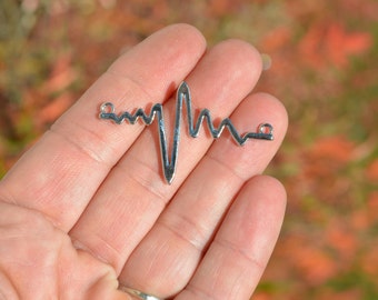 May include: Silver-toned metal charm shaped like a heart beat line. The charm has two jump rings for attaching to a necklace or bracelet.