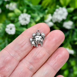 May include: Silver charm in the shape of a stylized elephant with a trunk raised in the air. The charm is small and detailed, perfect for adding a touch of whimsy to jewelry.