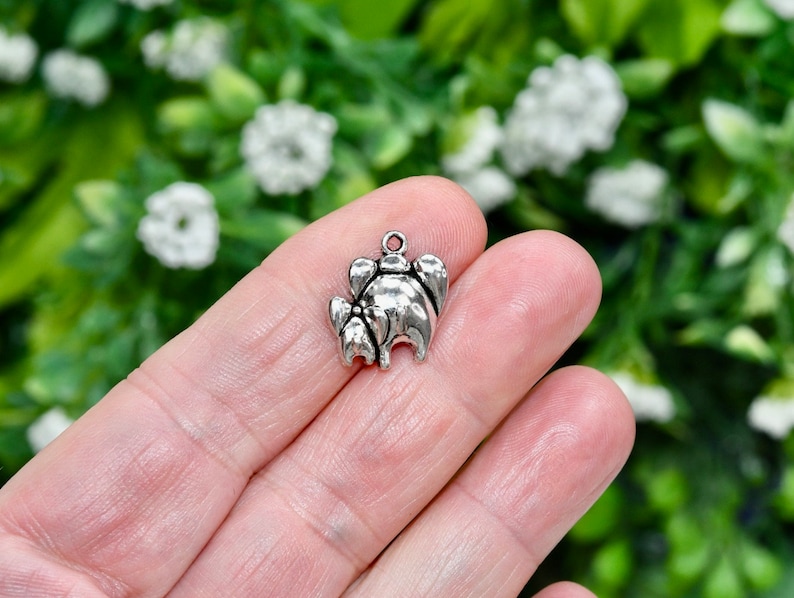May include: Silver charm in the shape of a stylized elephant with a trunk raised in the air. The charm is small and detailed, perfect for adding a touch of whimsy to jewelry.