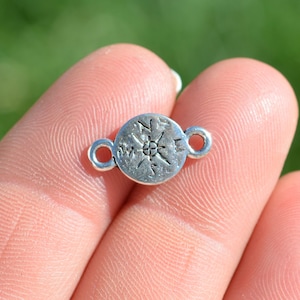 May include: Silver-toned compass charm with two jump rings. The compass features a north arrow and the letters N, S, E, and W.