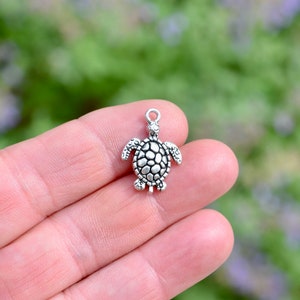 May include: Silver-toned turtle charm with a textured shell. The charm is small and detailed, perfect for jewelry making or crafting.
