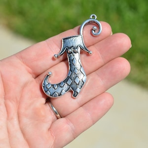 May include: Silver charm in the shape of a jester's shoe with a diamond pattern. The charm has a loop at the top for attaching to a necklace or bracelet.