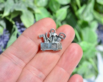 May include: Silver charm in the shape of a toolbox with various tools sticking out of the top. The tools include a hammer, saw, wrench, and screwdriver.