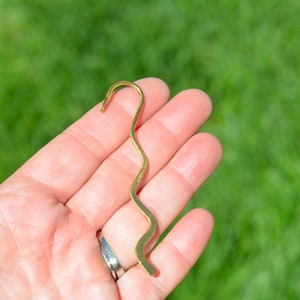 May include: A gold-colored metal bookmark with a wavy design. The bookmark is shaped like a hook at the top.