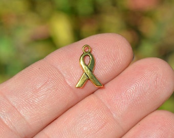 May include: Gold-colored metal ribbon charm. The ribbon is tied in a bow and has a loop at the top for attaching to a necklace or bracelet.