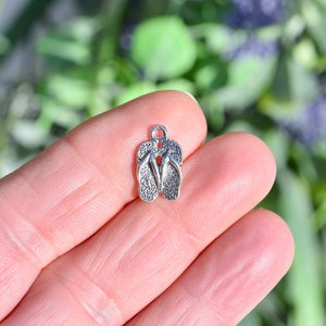 May include: Silver charm in the shape of a pair of flip flops.