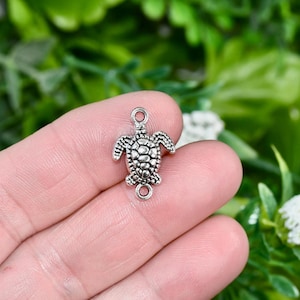 May include: Silver-toned turtle charm with a detailed shell design. The charm has two jump rings for attaching to jewelry or other crafts.