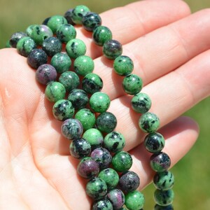 May include: A strand of green and black gemstone beads. The beads are round and have a smooth, polished finish.