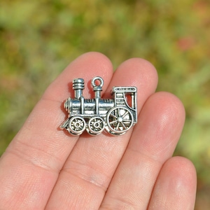 May include: Silver-toned metal charm shaped like a vintage train engine. The charm has a detailed design with wheels, a smokestack, and a caboose.