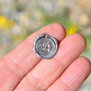 May include: Silver charm with a raised letter A in a wax seal design.