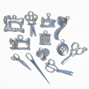 May include: A collection of silver-toned metal charms with sewing themes. The charms include a sewing machine, scissors, buttons, a spool of thread, and a measuring tape.