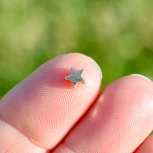 May include: A small, silver star charm held between two fingers.