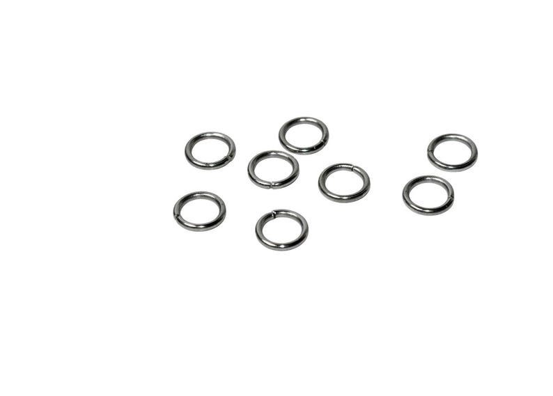 Op de afbeelding: Een verzameling van zeven kleine, ronde metalen buigringen met een gladde, gepolijste zilverkleurige afwerking. Elke ring heeft een enkele, dunne snede langs de omtrek, waardoor de ring geopend en gesloten kan worden om sieraden te verbinden.