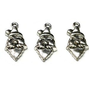 May include: Three silver-toned Santa Claus charm pendants with a red nose and white beard. The charms are in the shape of a Santa Claus head with a hat.