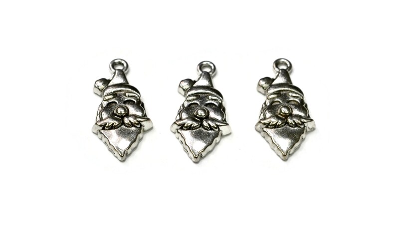 May include: Three silver-toned Santa Claus charm pendants with a red nose and white beard. The charms are in the shape of a Santa Claus head with a hat.