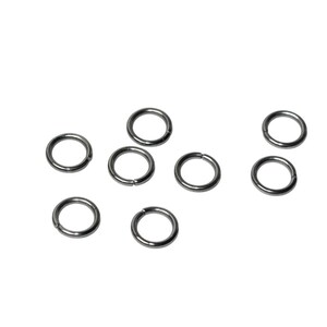 May include: A collection of seven small, circular metal jump rings with a dark gunmetal finish. Each ring features a single, clean cut along its circumference, allowing the ring to be opened and closed for connecting jewelry components.