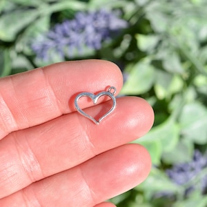 May include: A silver open heart charm pendant with a loop at the top for attaching to a necklace or bracelet.