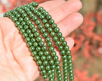 May include: A strand of green glass beads, with a high gloss finish, are displayed on a hand. The beads are round and uniform in size.
