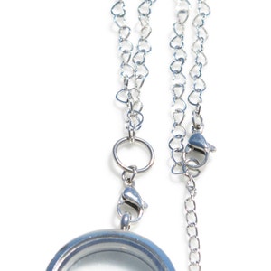 May include: A silver locket necklace with a heart-shaped chain. The locket has a clear glass insert and a silver chain attached to the top.