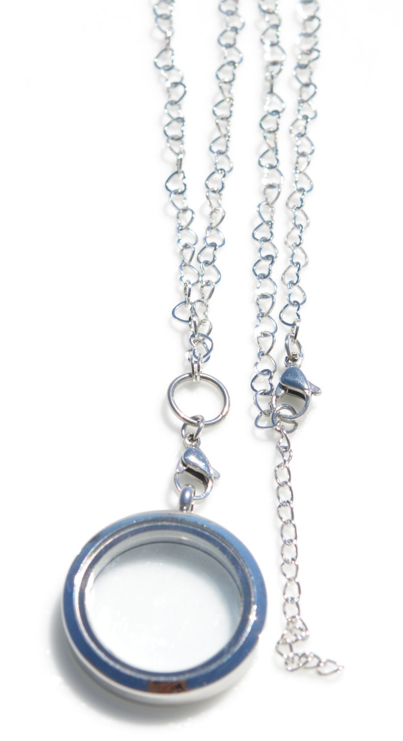 May include: A silver locket necklace with a heart-shaped chain. The locket has a clear glass insert and a silver chain attached to the top.