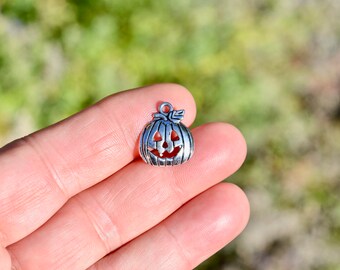 May include: Silver charm in the shape of a jack-o'-lantern pumpkin with a carved face.