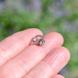 May include: A silver ring with a clear gemstone in the center.