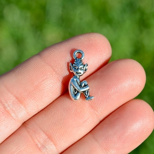 May include: A silver charm in the shape of a small, seated, mythical creature with pointed ears and a long tail.
