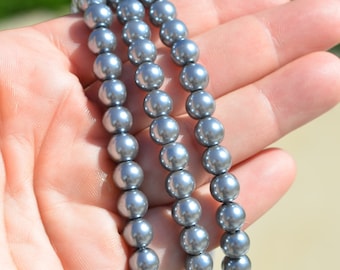 May include: Strands of gray pearl beads. The beads are round and have a shiny, reflective surface. The beads are held in a hand, with the background out of focus.