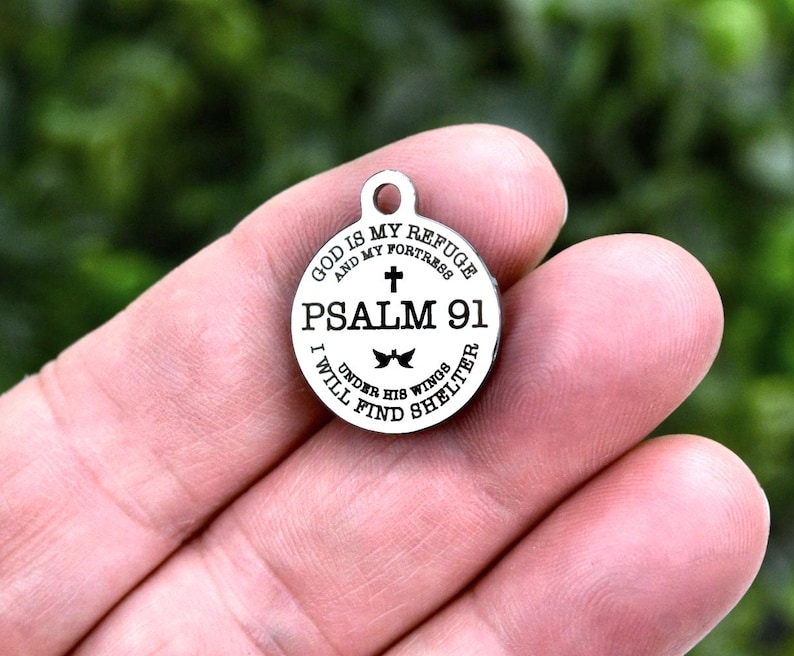 May include: A silver-colored round pendant with the text "GOD IS MY REFUGE AND MY FORTRESS PSALM 91 I WILL FIND UNDER HIS WINGS SHELTER" encircling a cross and a bow tie design. The pendant has a small loop at the top.