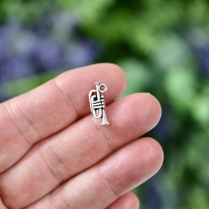 May include: Silver trumpet charm pendant. The charm is small and detailed, with a realistic trumpet design.