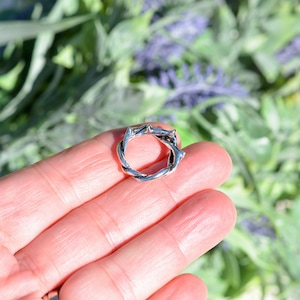 May include: A silver ring shaped like a twisted thorn crown.