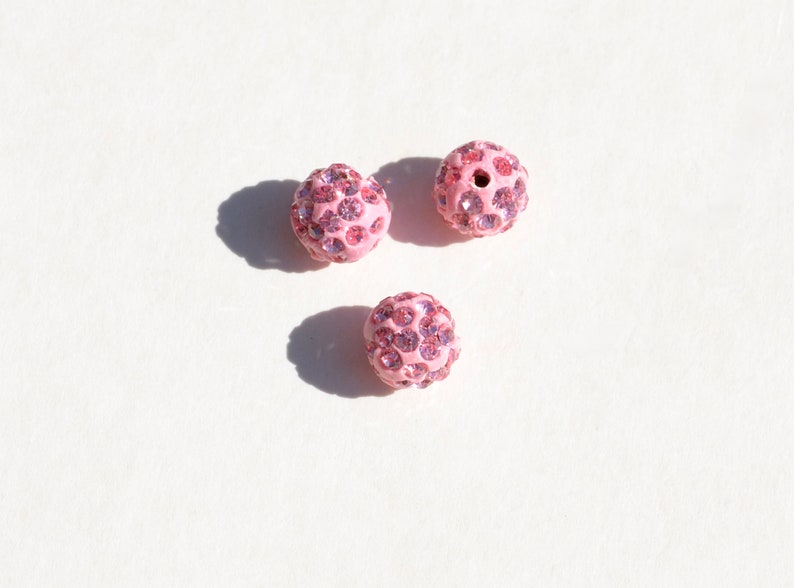 May include: Three pink round beads with a sparkly finish. Each bead is covered in small pink rhinestones.