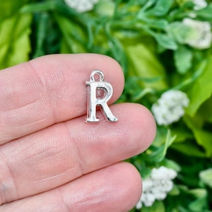 May include: Silver charm with the letter R. The charm is in the shape of the letter R and has a loop at the top for attaching to a necklace or bracelet.