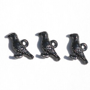 May include: Three black metal crow buttons with a loop for sewing on. The crows are in a standing position with their wings slightly spread.